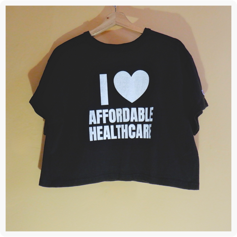 I Love Affordable Healthcare black crop top with bold white lettering hanging on a wooden hanger