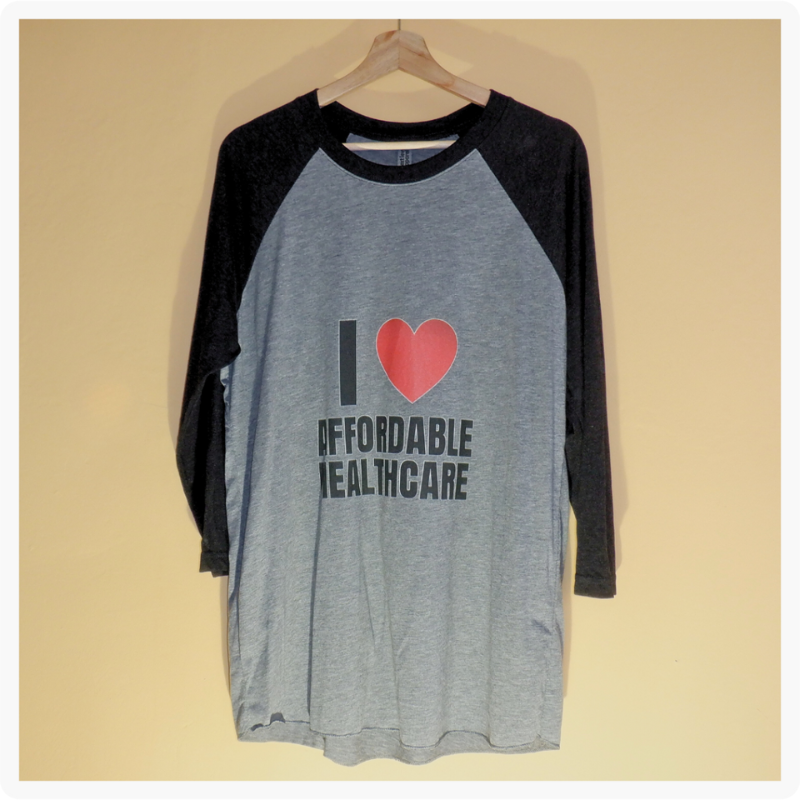 I Love Affordable Healthcare grey and black raglan 3/4 sleeve shirt hanging on a wooden hanger